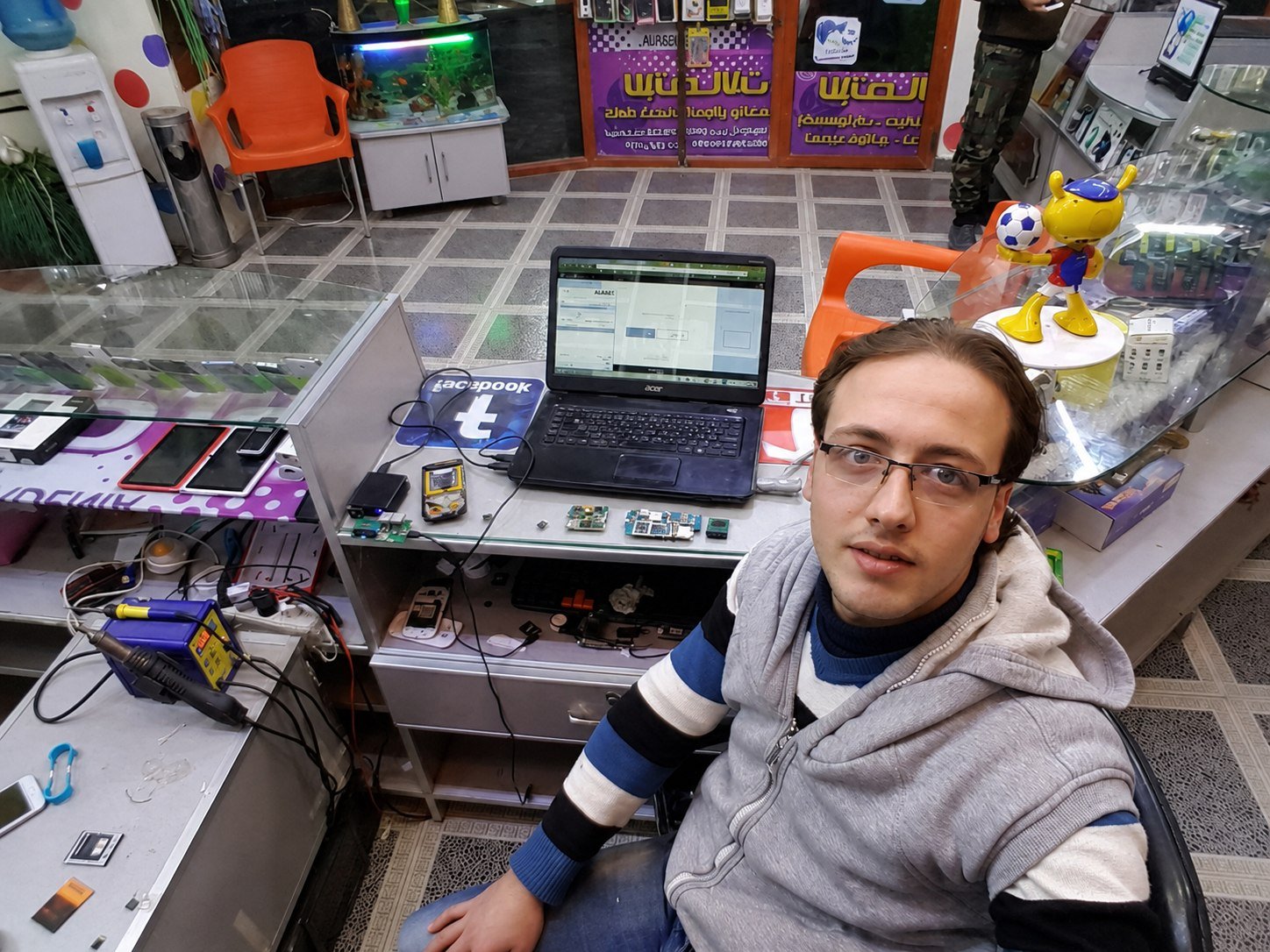 Basel at a repair bench in his first phone shop, soldering station and laptop around him.