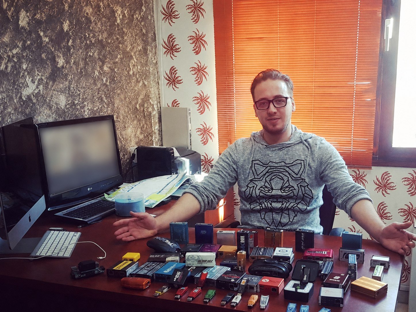 Basel at a desk spread with repair tools and dongles, arms open.