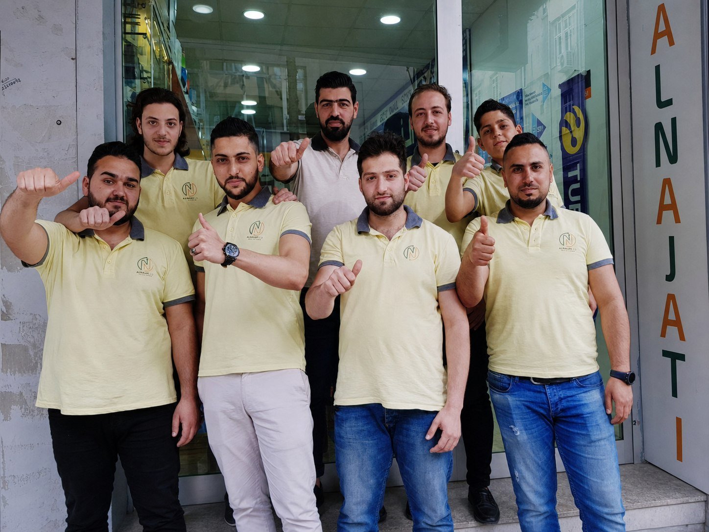 Basel with his team outside the shop, everyone giving a thumbs-up.