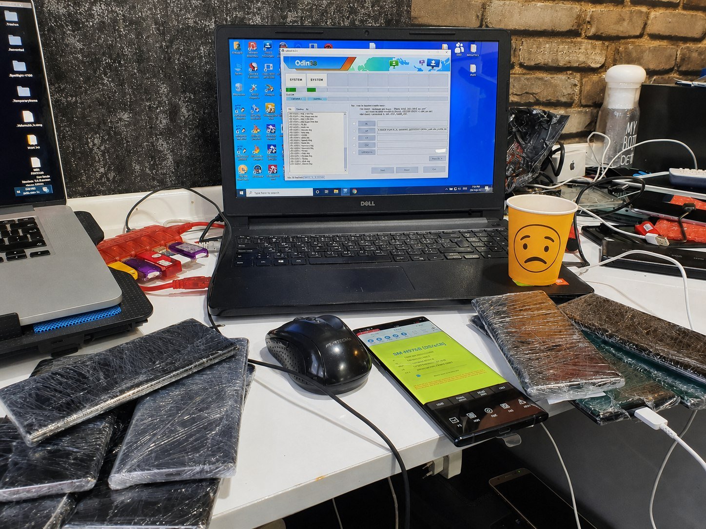 A laptop running flashing software amid wrapped phones — the detail work of IMEIRadiX.