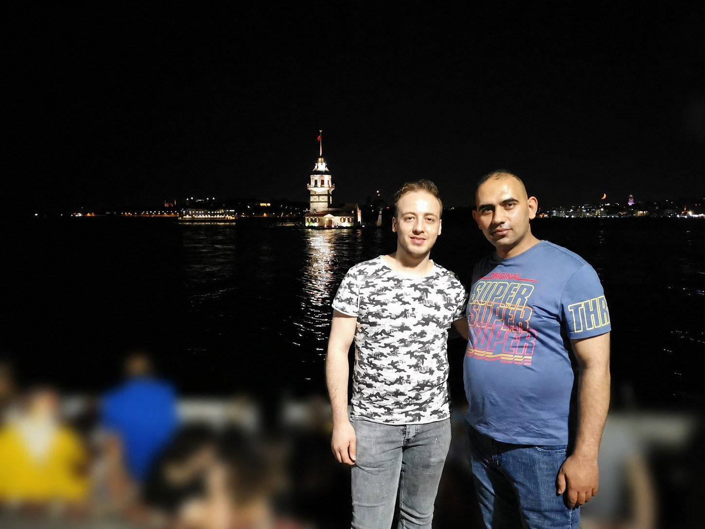 Basel and his business partner by the Bosphorus at night, Maiden's Tower behind them.